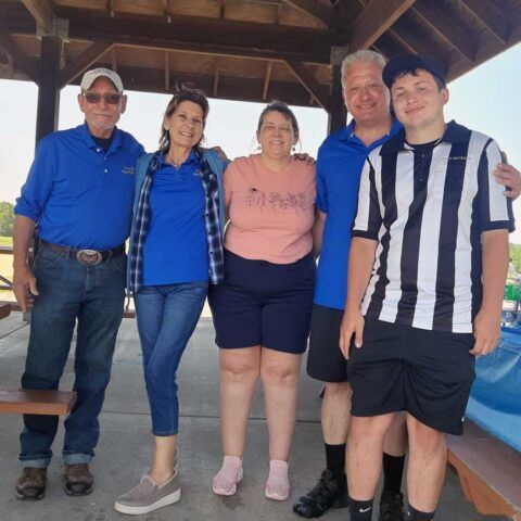 Five people posing together under a wooden pavilion, smiling at the camera.