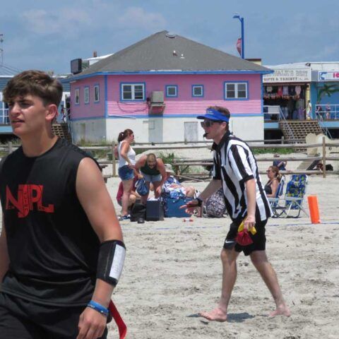 People at a beach, with a pink house and spectators in the background.