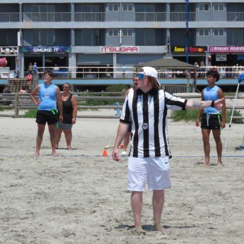 People standing on a beach, with a player in a black-and-white striped shirt in the foreground.