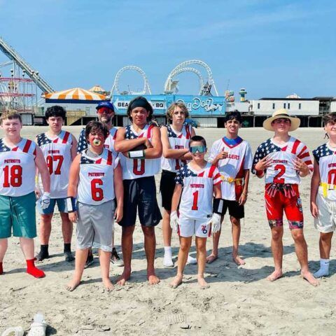 Group of beach football players posing in jerseys on a sandy beach with amusement rides in the background