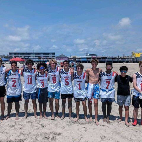 Group of football players posing on a sandy beach, wearing white jerseys with red numbers.