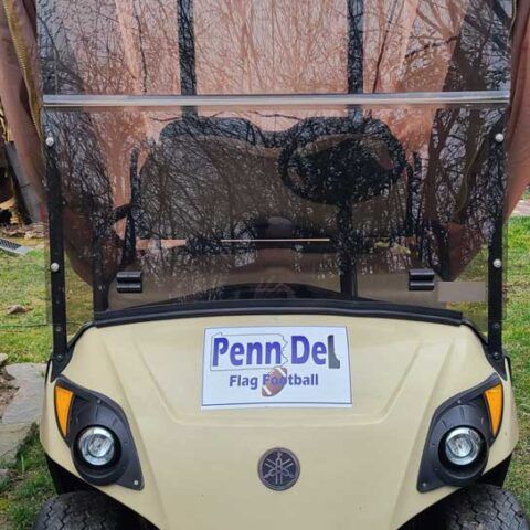 Yellow golf cart with a Penn Del Flag Football sign parked outdoors under bare trees