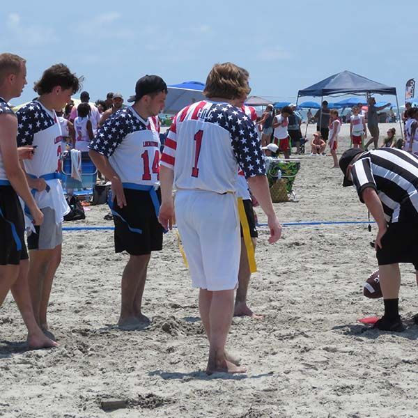 People in matching jerseys stand on a beach, gathered for a sports game under blue skies.