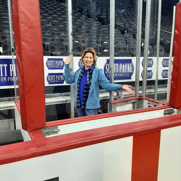 Woman smiling and posing behind a red hockey rink penalty box