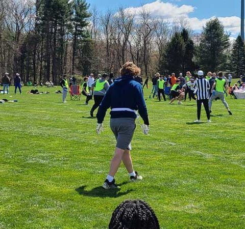 People playing football on a grassy field in a park on a sunny day