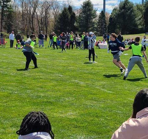 People playing football on a grassy field in a park on a sunny day