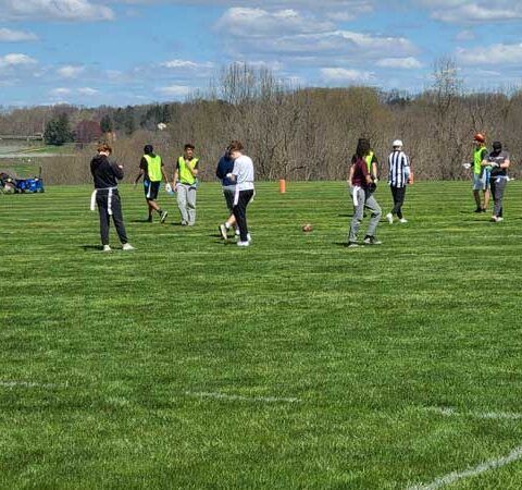 People standing on a grassy field during an outdoor sports game on a cloudy day