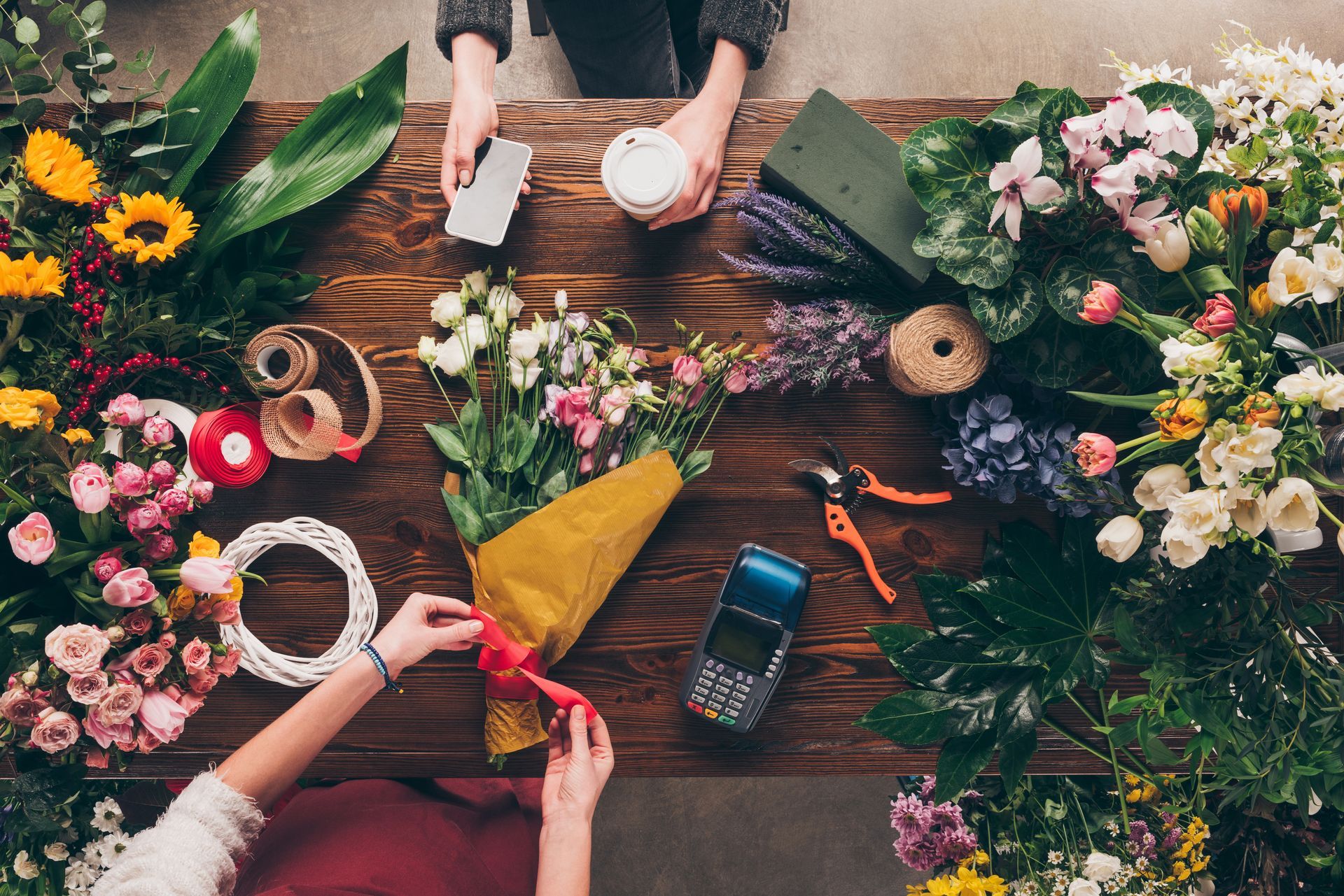 Creative florist arranging fresh colorful blossoms and greenery bouquets on a rustic wood desk.