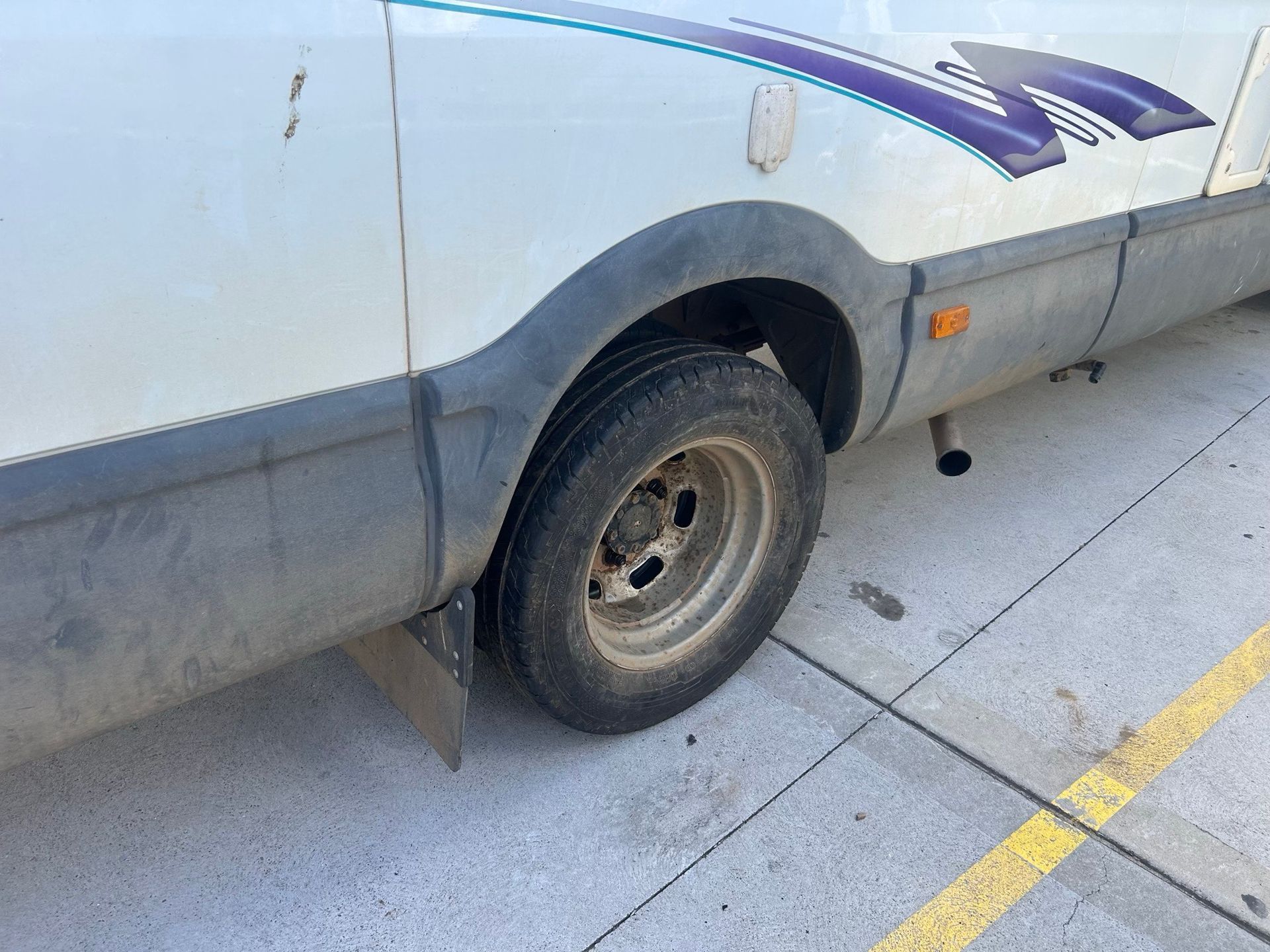 Side view of a white van’s rear wheel and lower body on a parking lot curb.