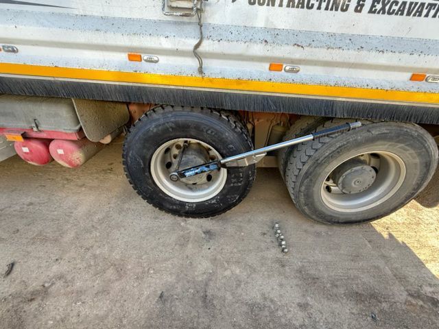 Truck trailer with two wheels, one flat tire, parked on concrete near a yellow line