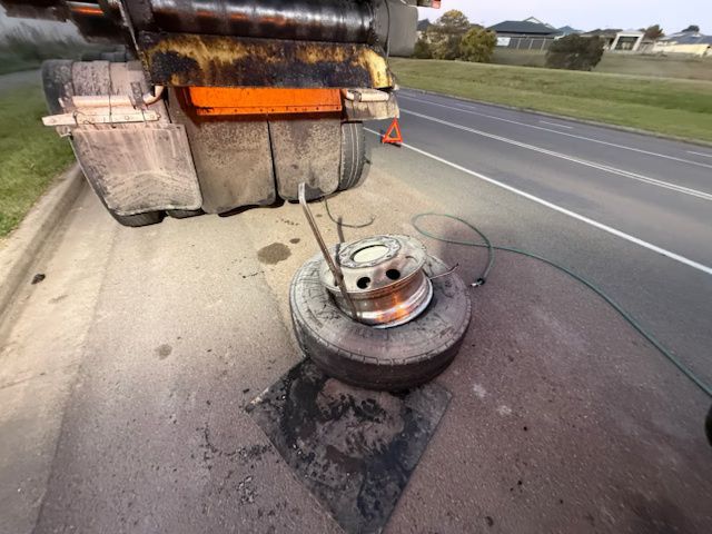 Disabled truck wheel on roadside with a detached tire and hose on the shoulder