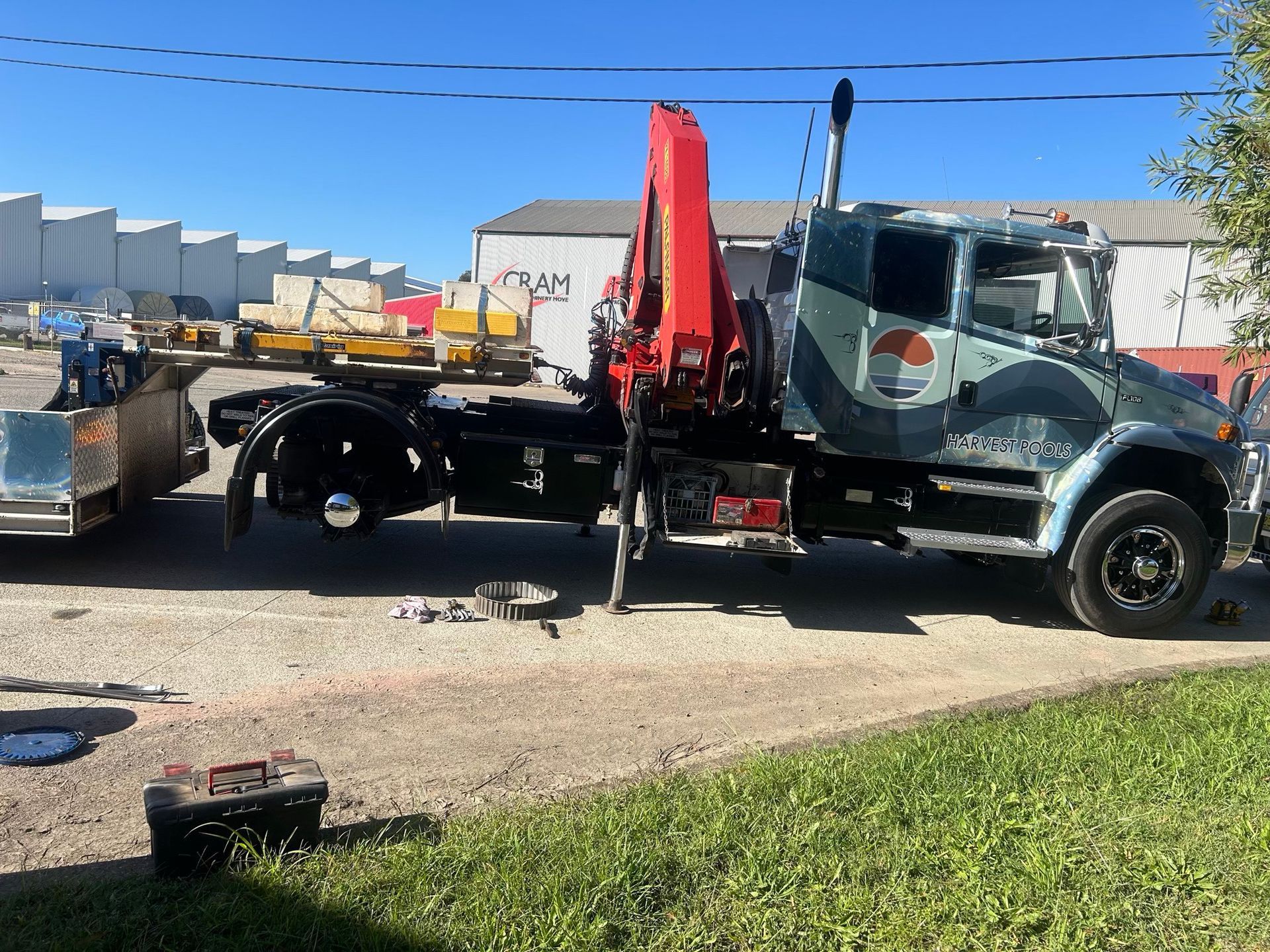 Tow truck with red crane lifting a black truck on a roadside under a clear sky