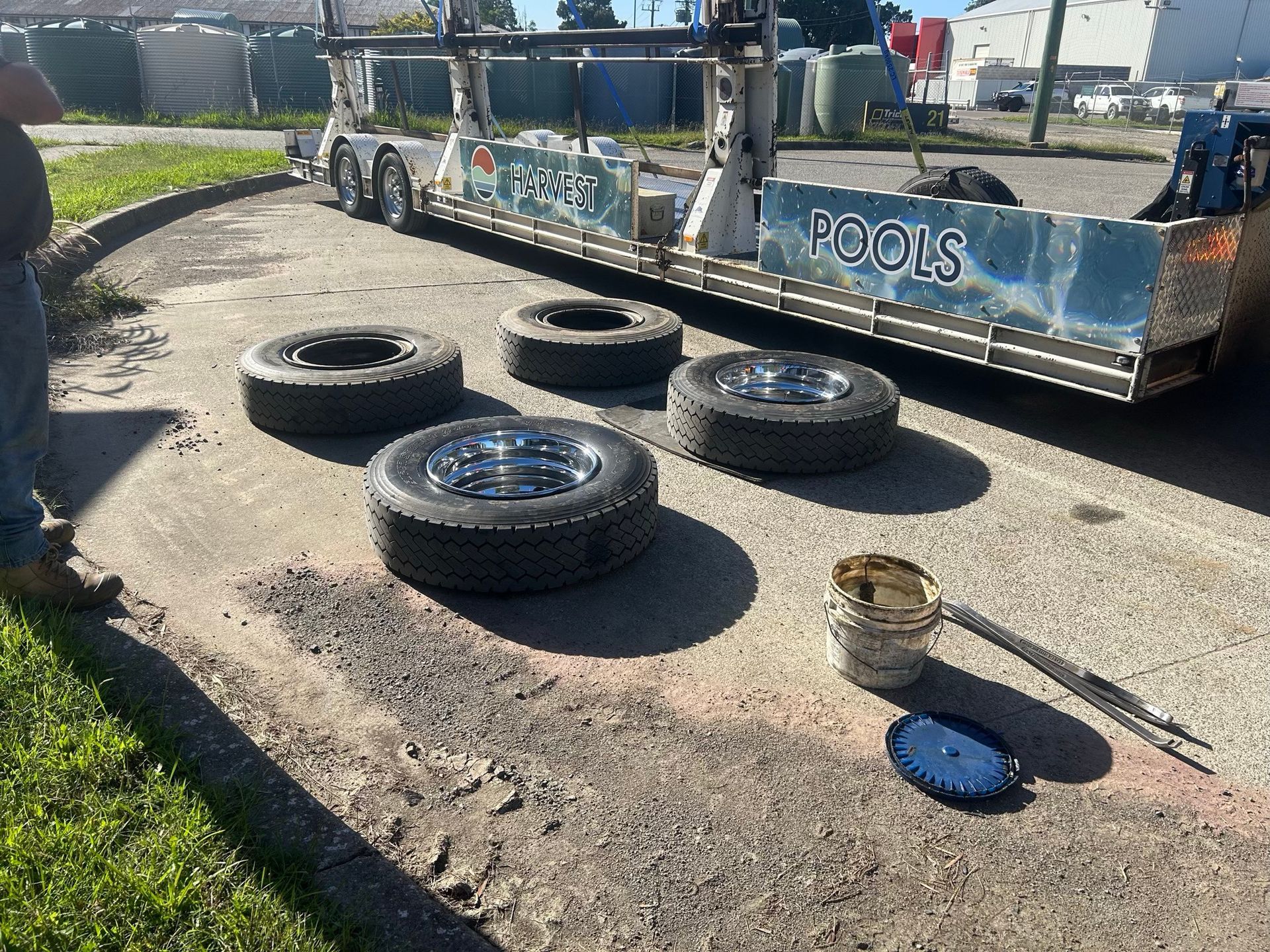 Five tires on pavement beside a trailer with colorful pool graphics and tools on the ground
