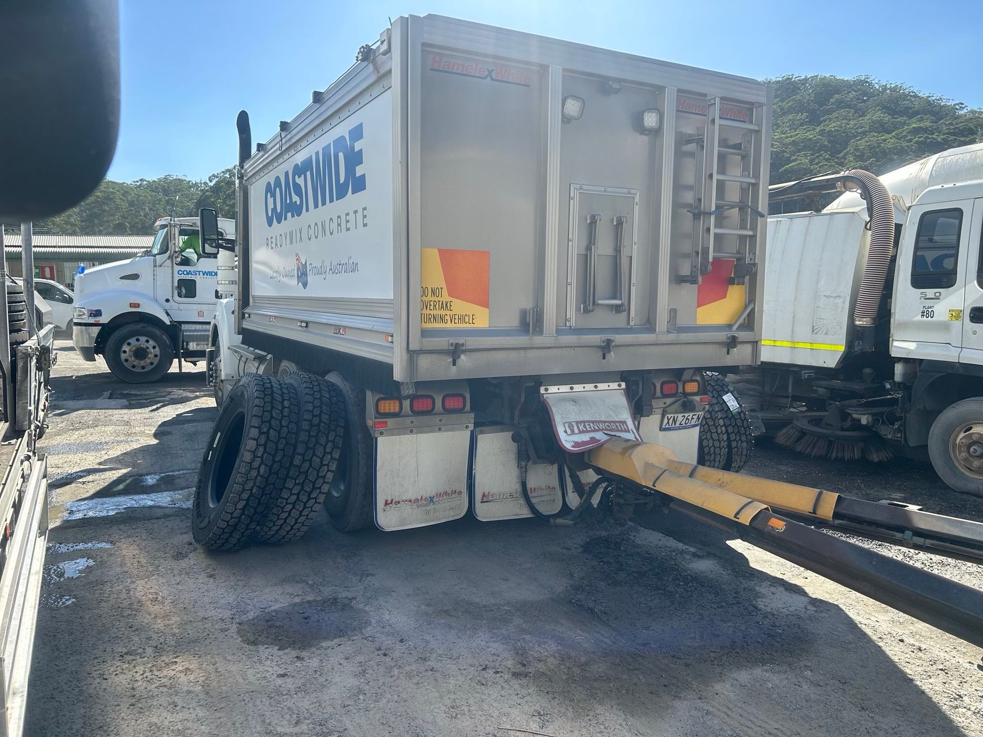 Damaged white utility truck with rear axle issue, parked in a lot with other trucks nearby