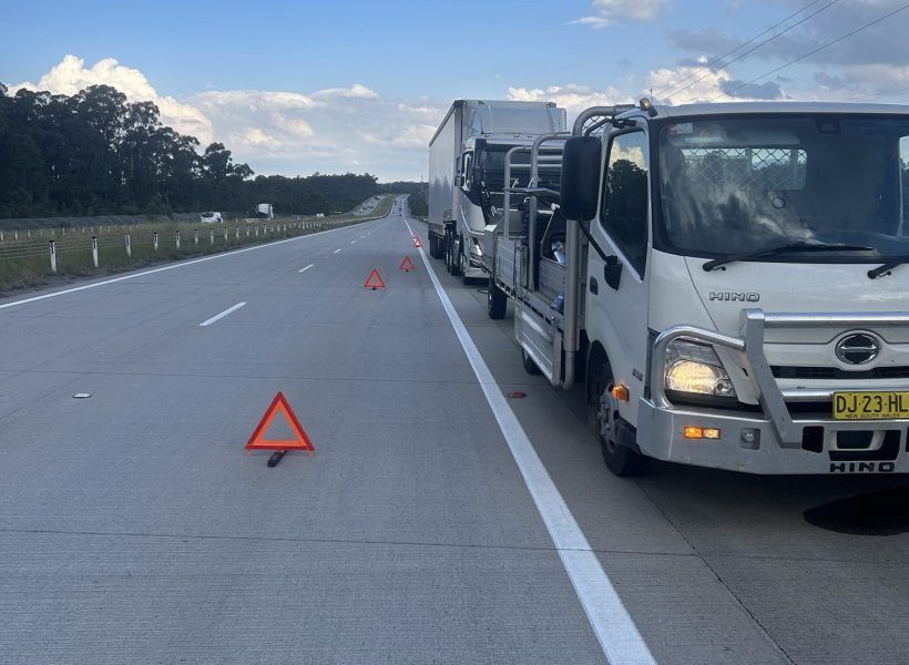 Trucks stopped on a highway shoulder with warning triangles placed behind them at dusk.