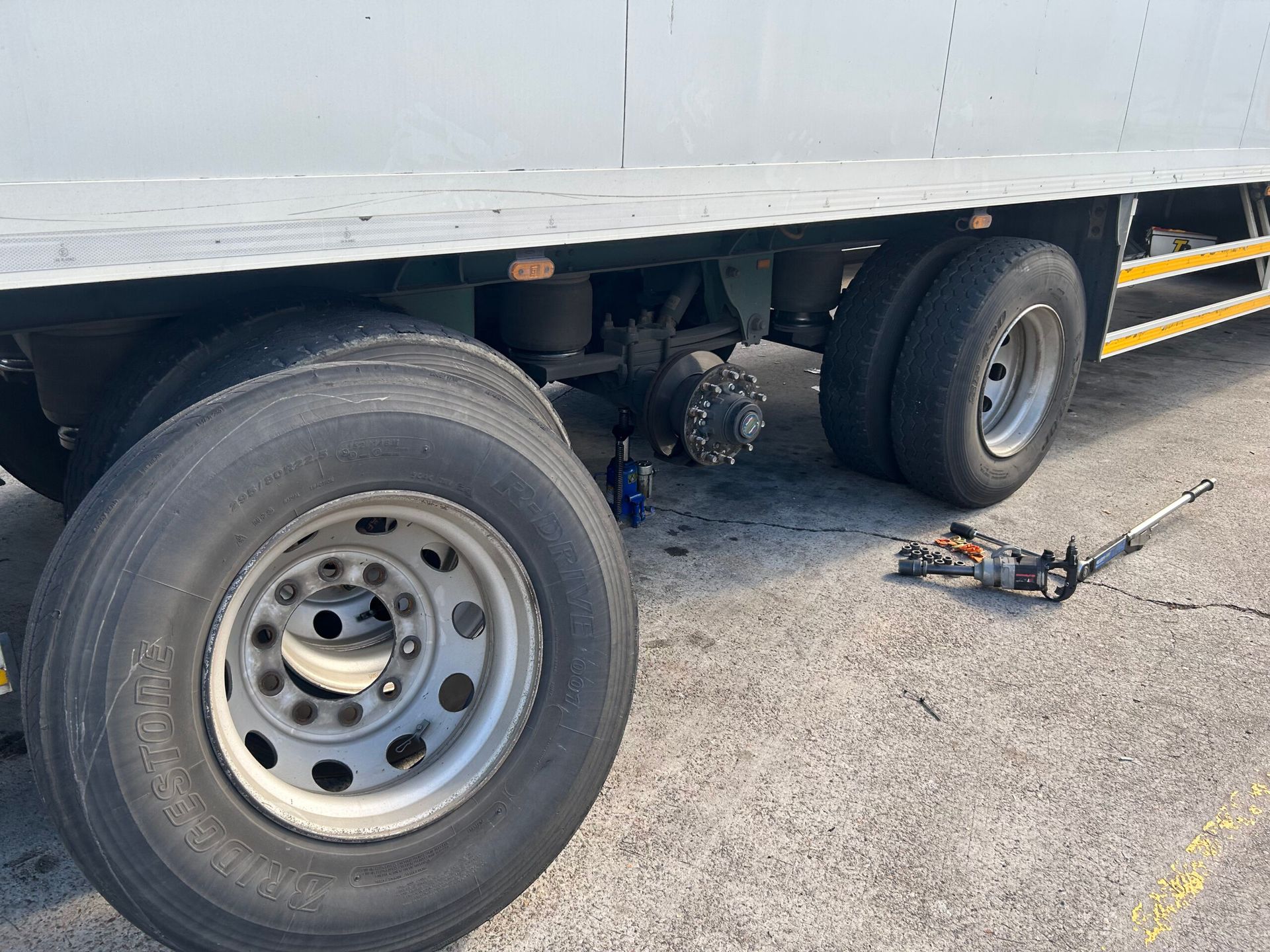 Semi-truck with rear wheel area exposed; a jack and tools sit on the pavement beside it.