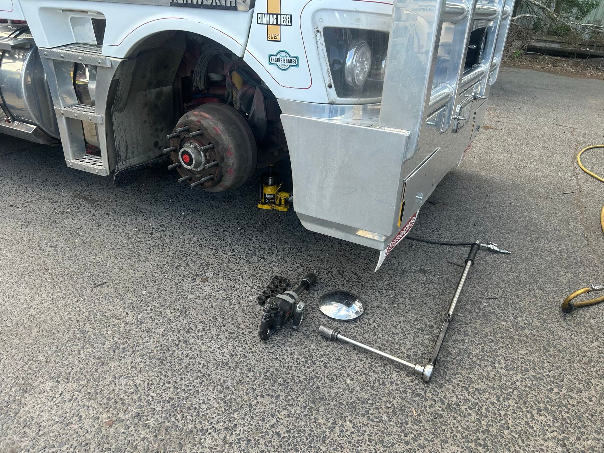 Damaged car front wheel and bumper on pavement, with loose parts and tools scattered nearby