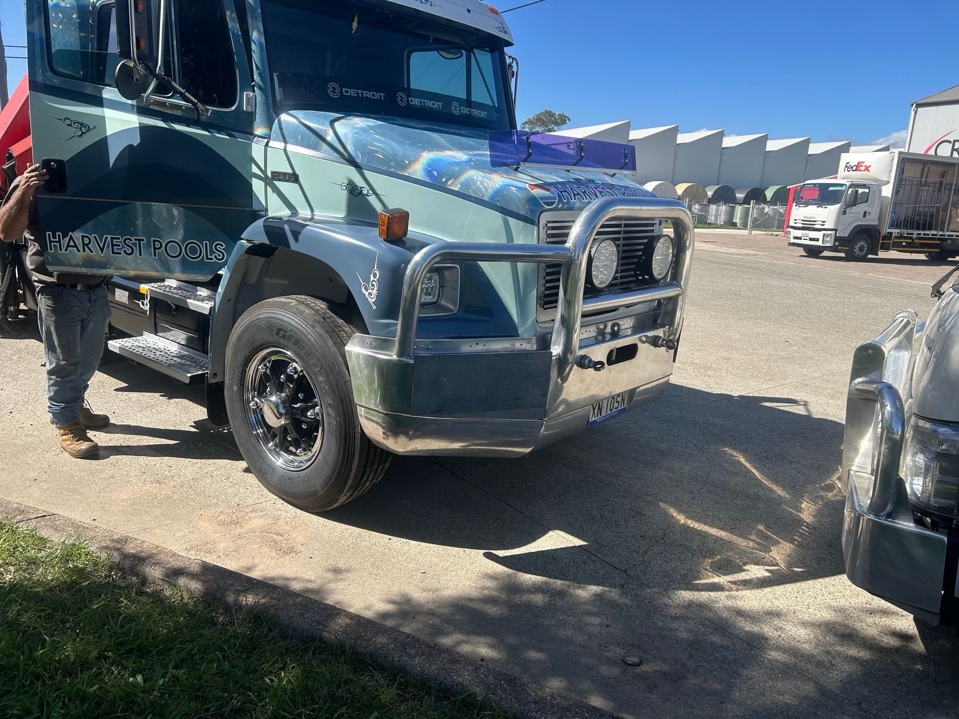 Dark green semi truck with a chrome grille parked on a gravel lot under a blue sky