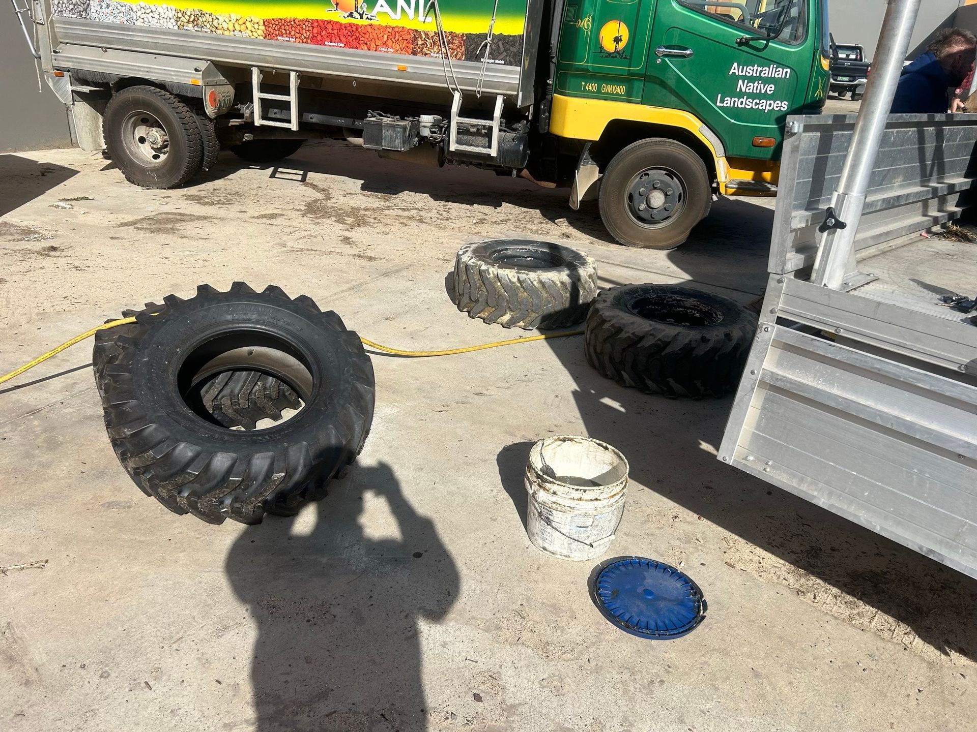 Several tires and tools on a dusty roadside beside a green truck and metal trailer.