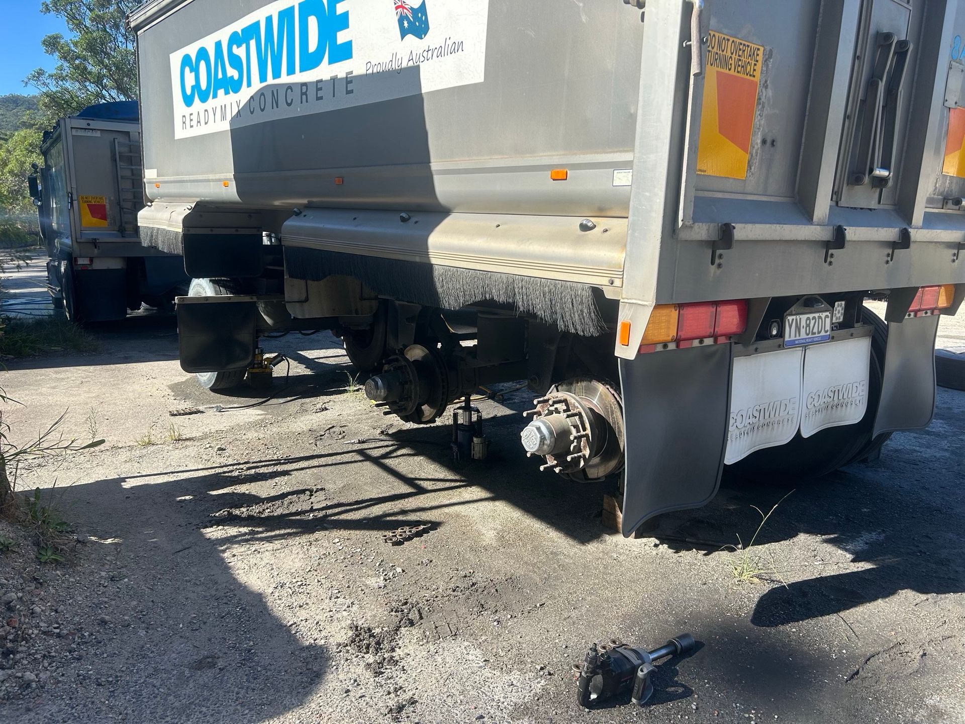 Damaged truck parked on gravel, with debris under the rear axle and a detached wheel nearby.