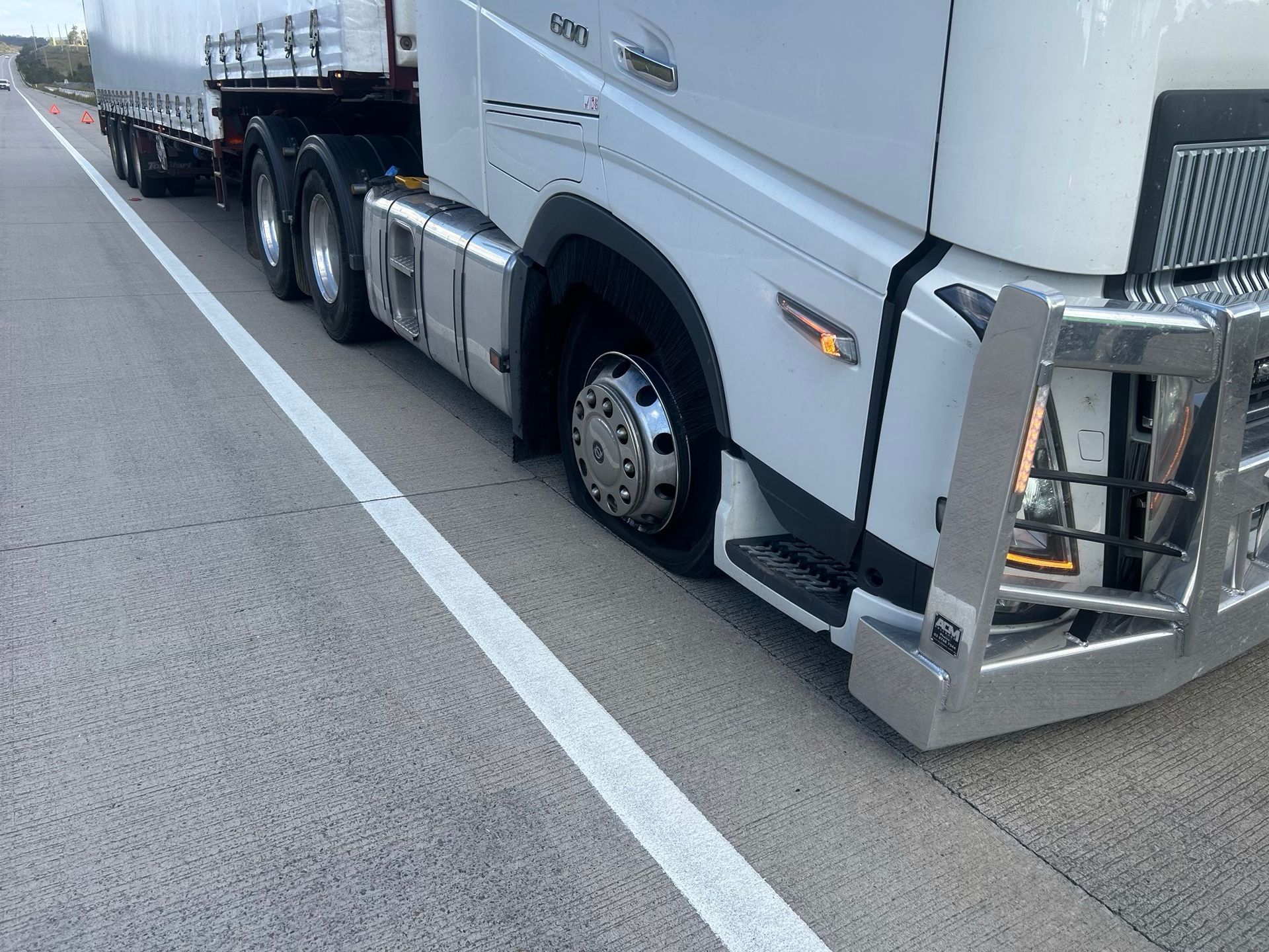 White semi-truck parked along a roadside, viewed from the front side near the lane line.