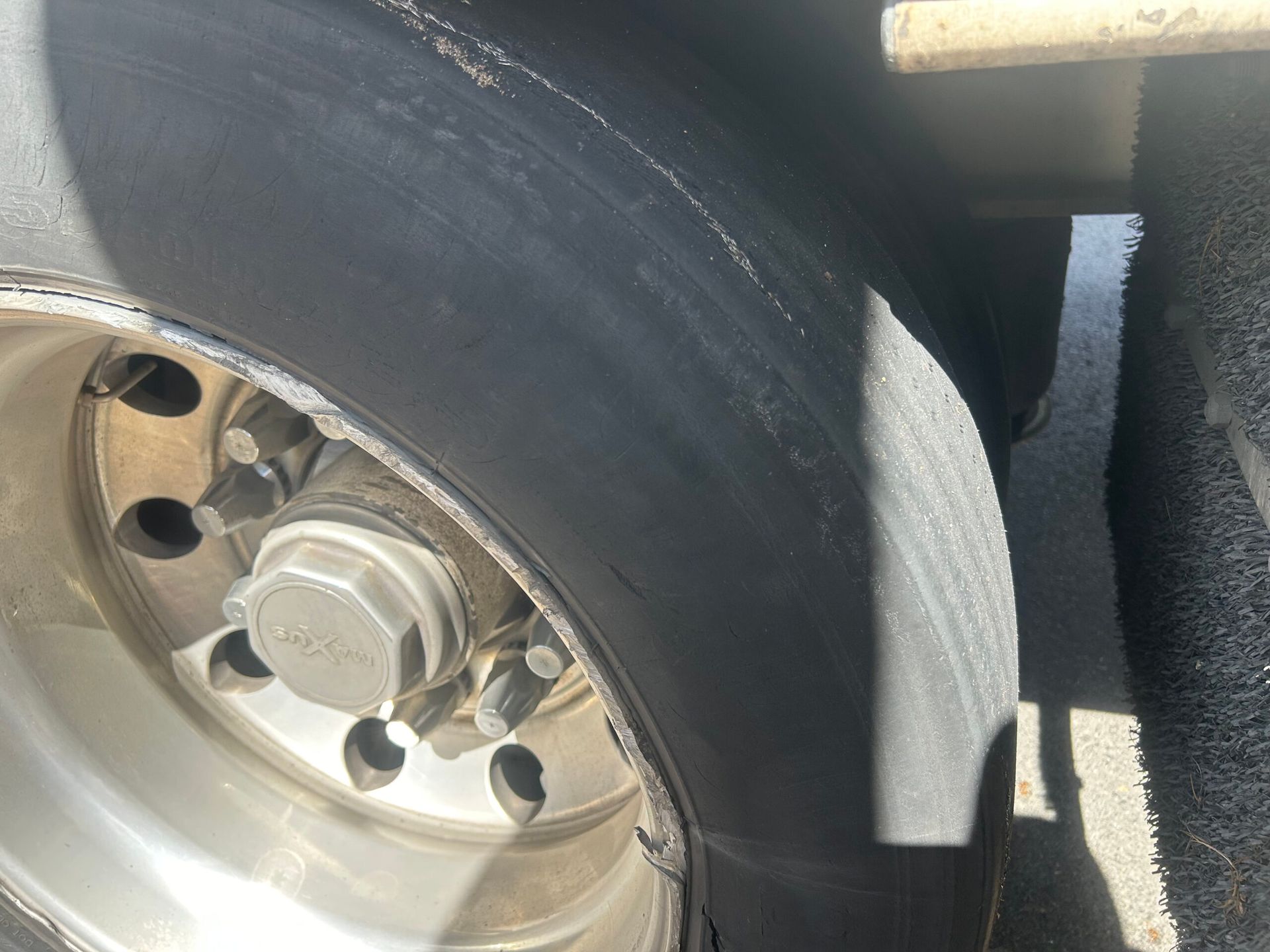 Close-up of a truck wheel and tire with a metal rim and lug nuts, showing worn tread and a mud flap.