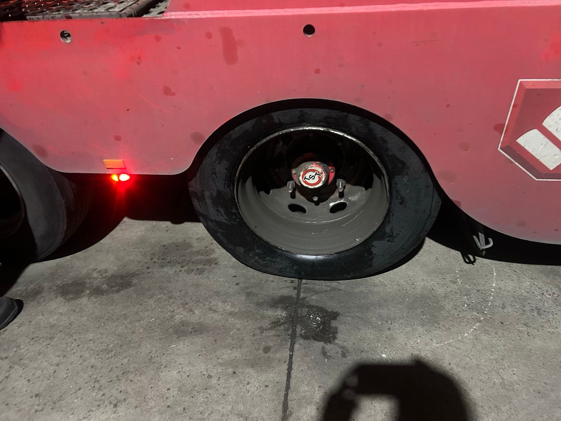 Red vehicle with a damaged wheel and flat tire parked on concrete at night