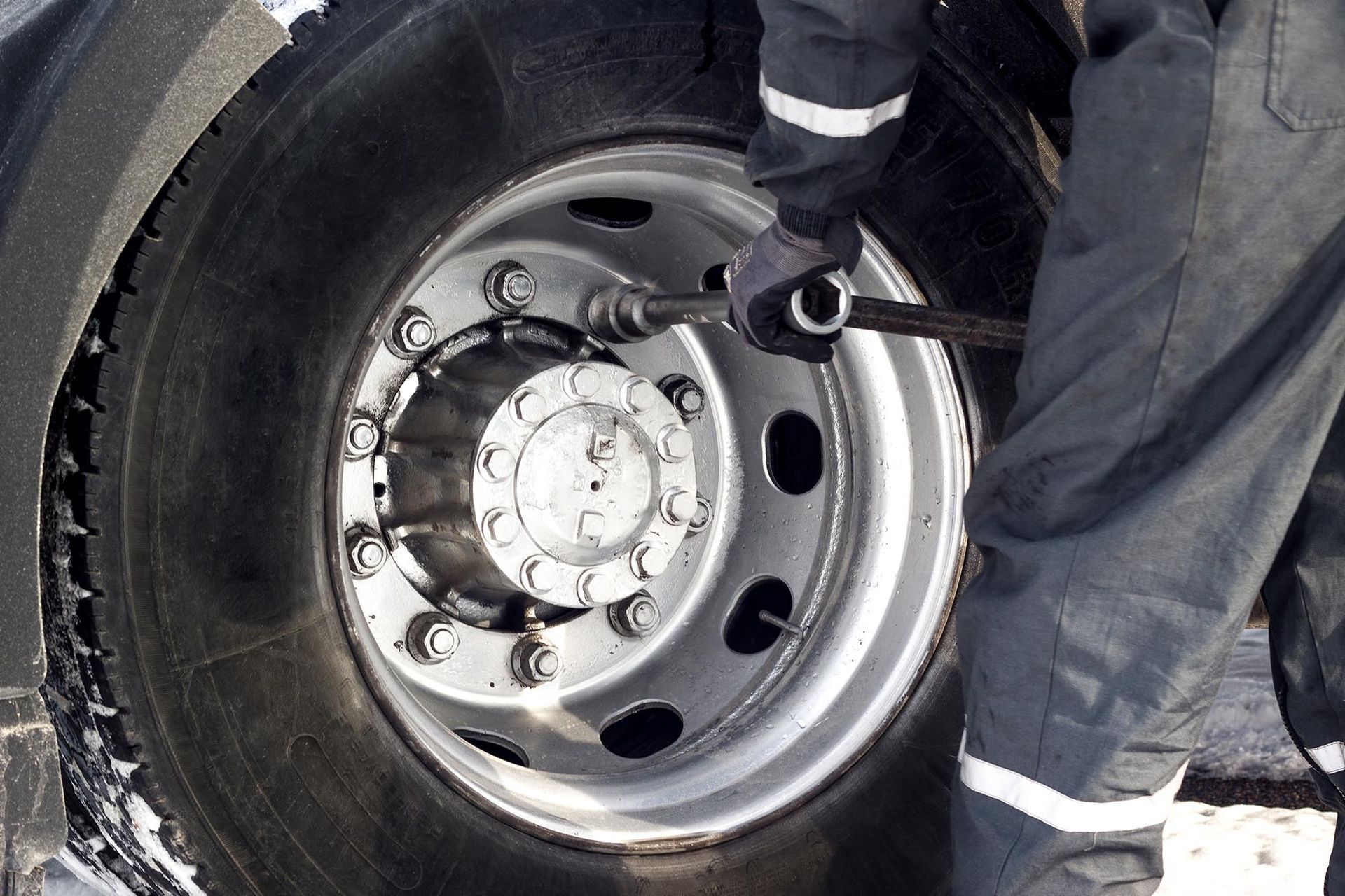 Mechanic inspecting a truck wheel and lug nuts in snowy conditions