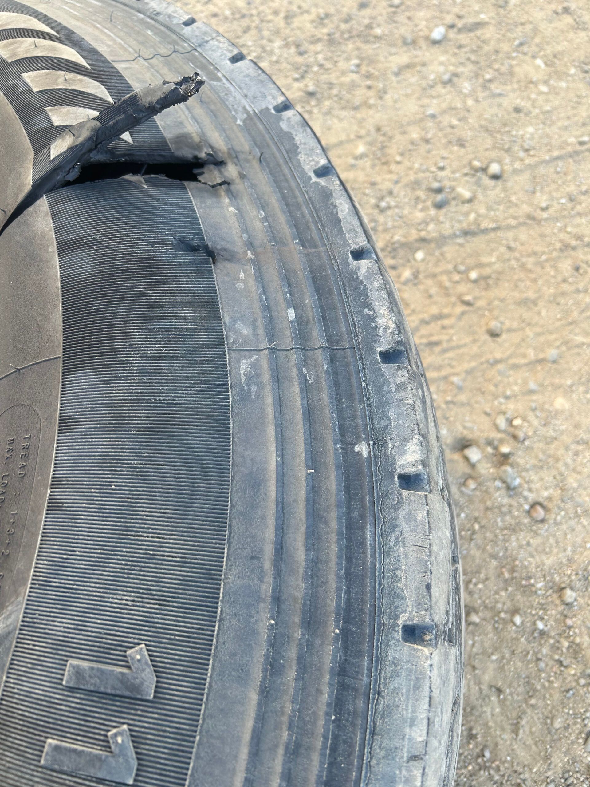 Close-up of a worn black tire sidewall on a dirt surface, with scuffs and tread detail visible