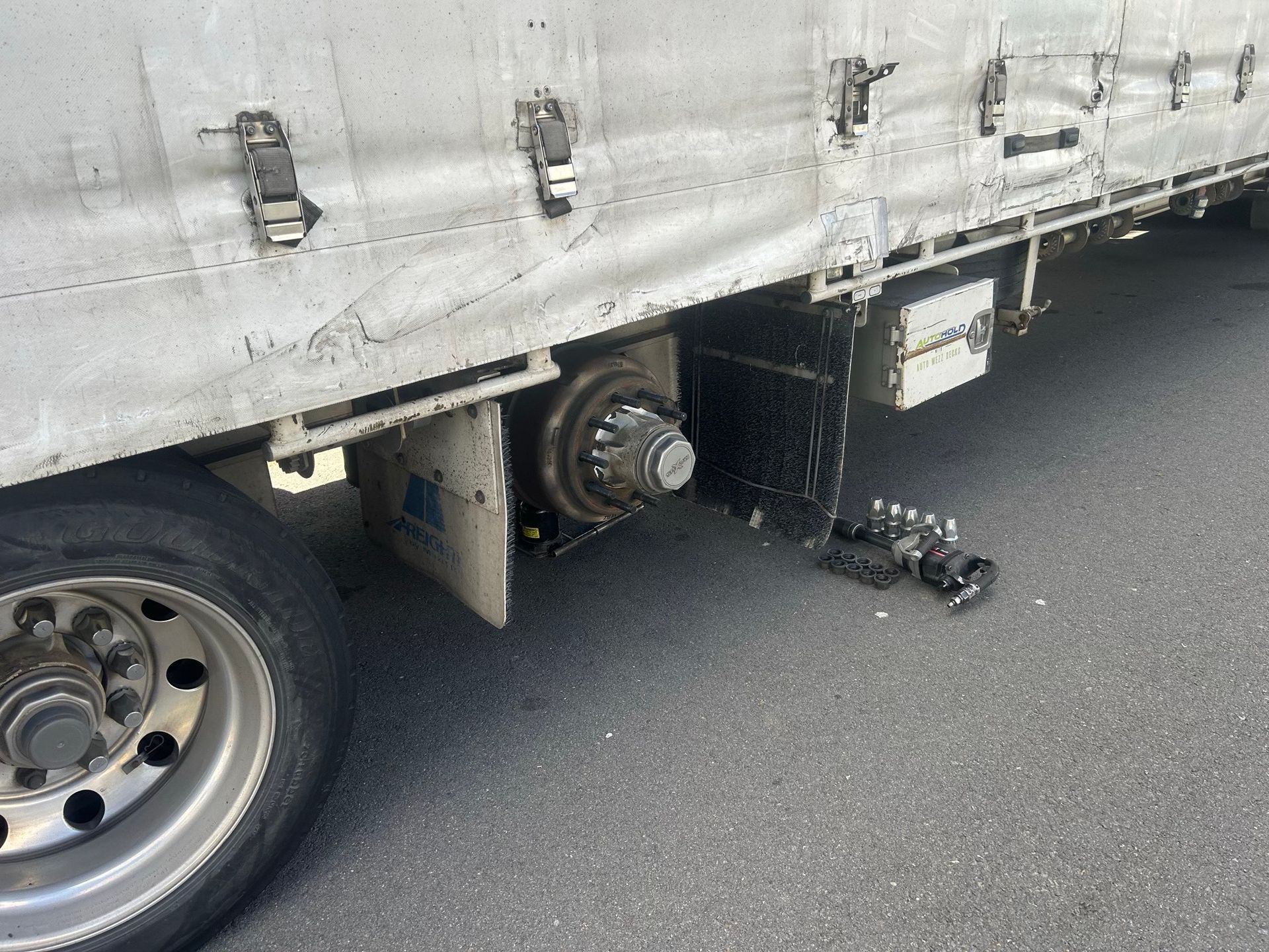 Damaged truck wheel and axle with detached parts under a white trailer on pavement