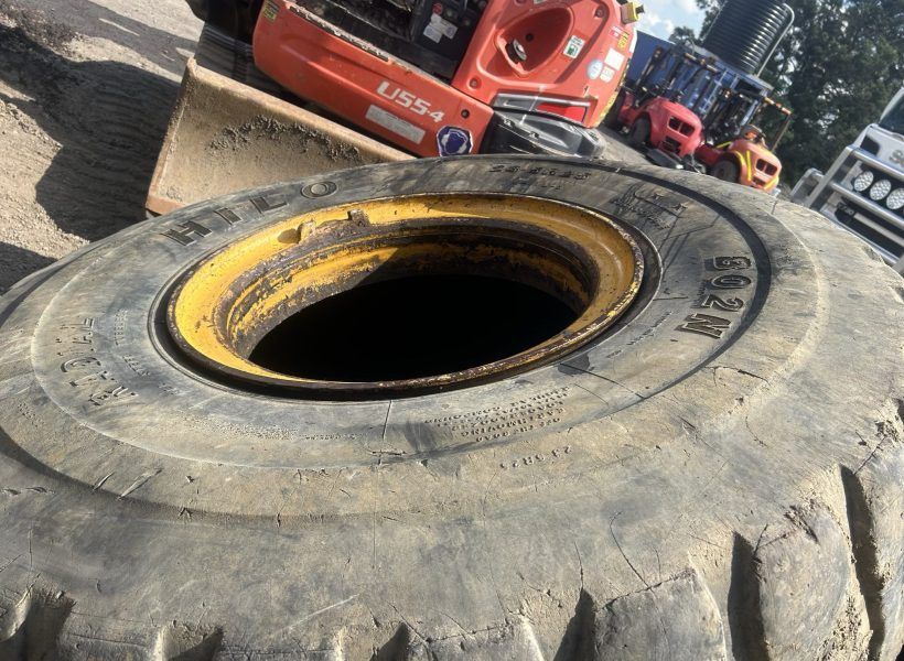 Large off-road tire lying on a dirt lot with red machinery in the background