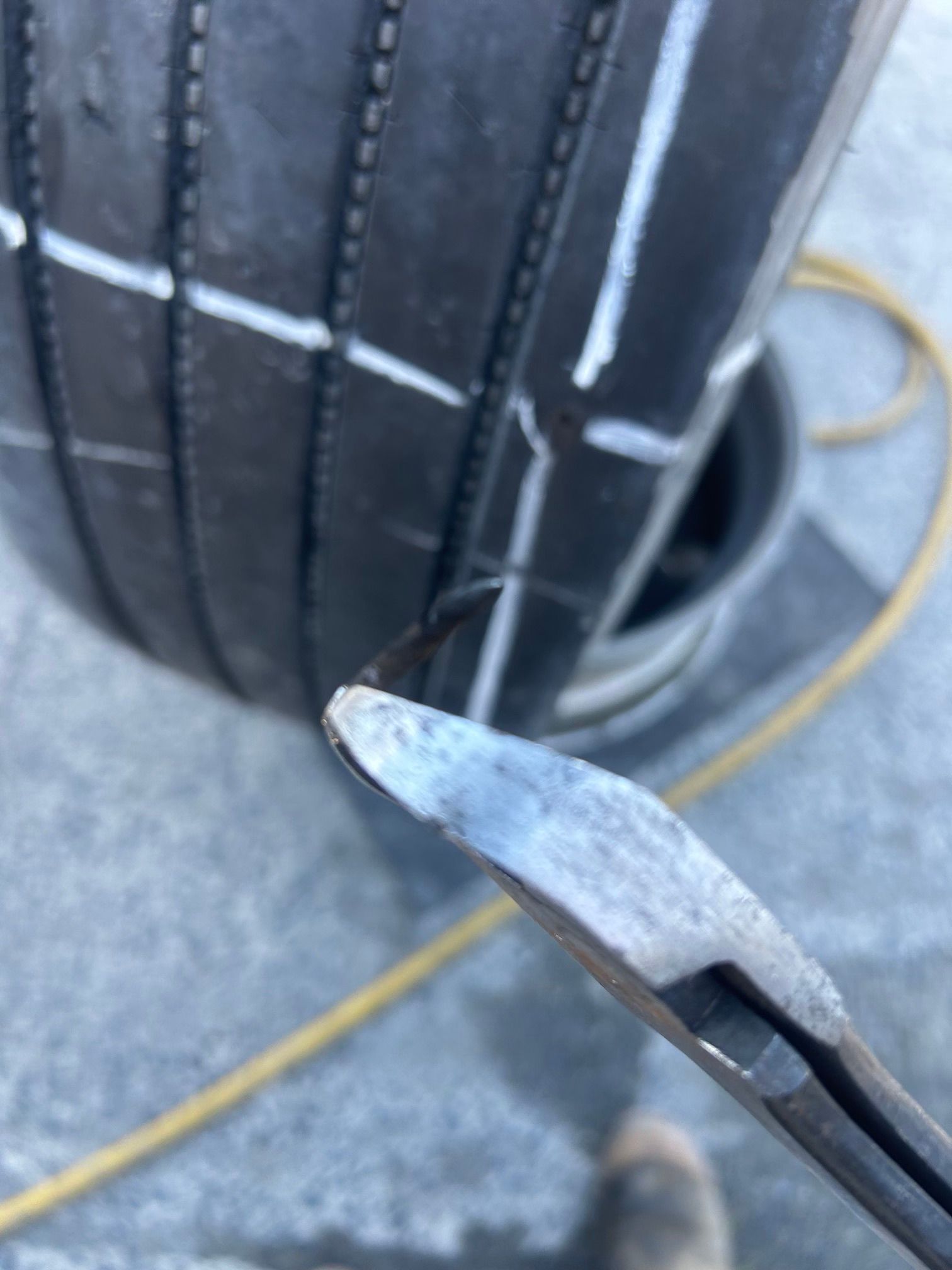 Close-up of a metal tool tip near a black tire or hose on a gray concrete floor.