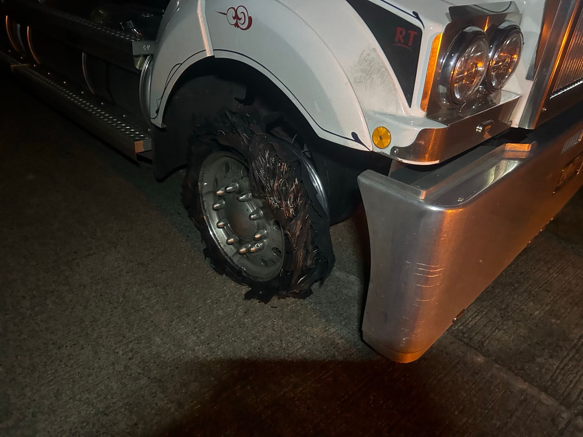 White truck with a damaged front tire and side panel at night, parked on pavement.