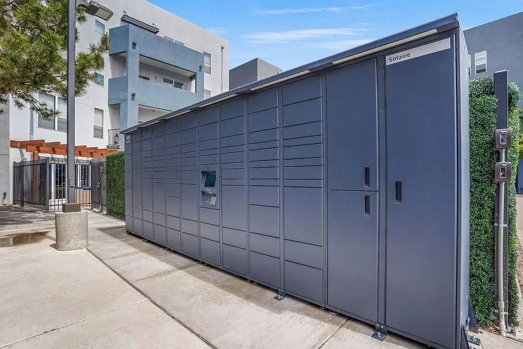 Large blue-gray utility cabinets along a sidewalk beside a modern building and fence at Solaire, offering apartments in Albuquerque, NM.