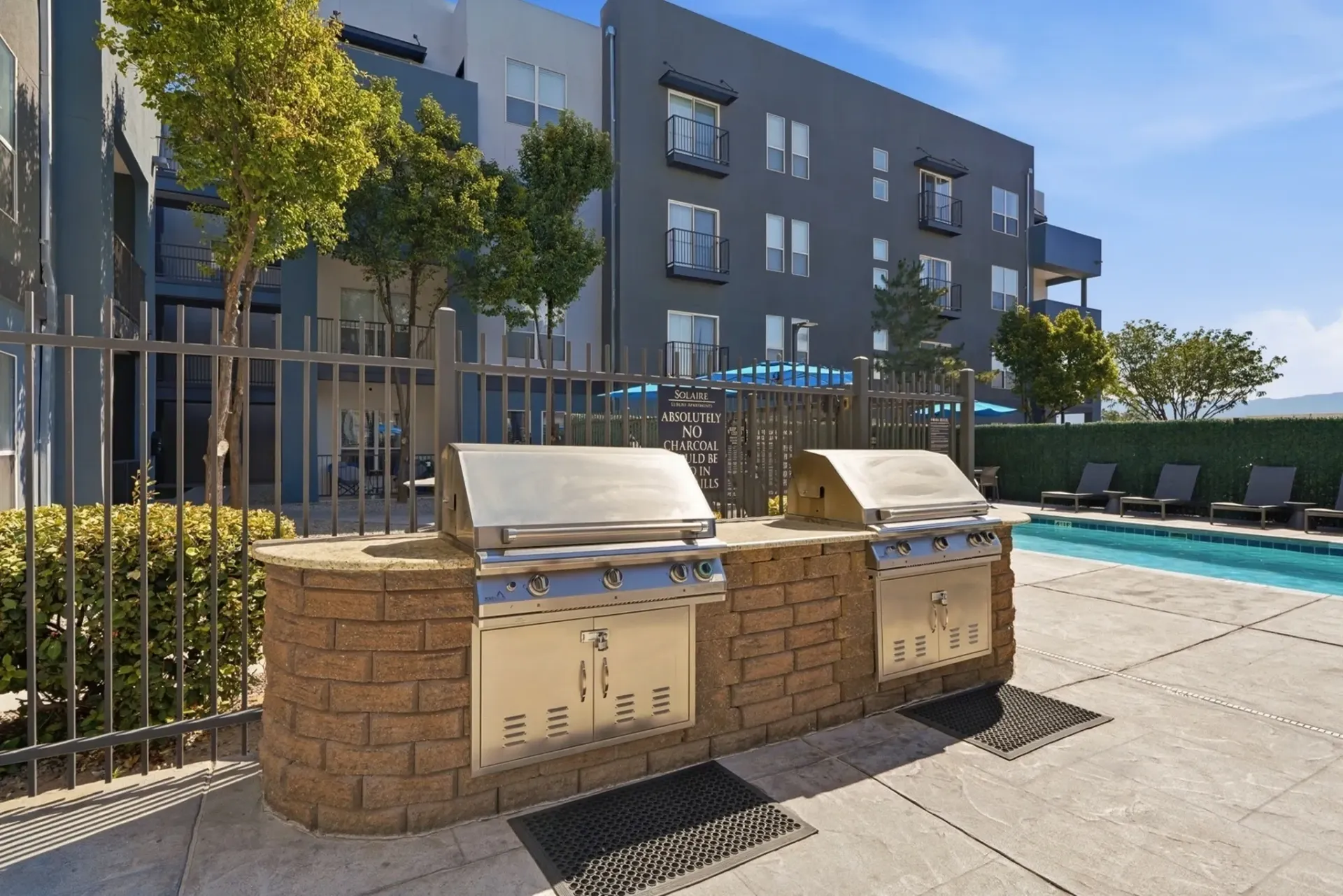 Outdoor grills next to a swimming pool with lounge chairs at a multifamily property at Solaire, offering apartments in Albuquerque, NM.
