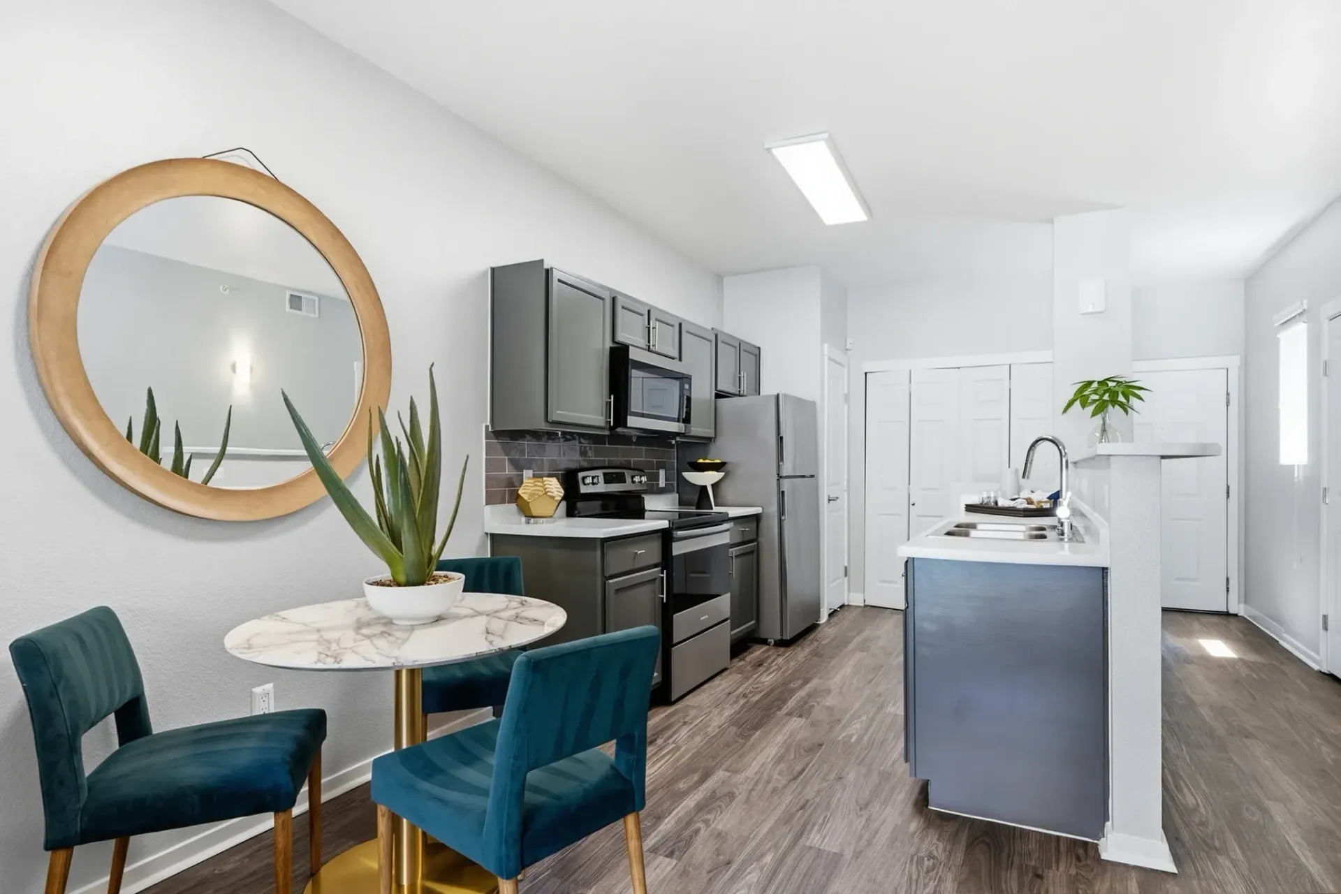 Modern kitchen with gray cabinets, stainless steel appliances, and a small dining area with two teal chairs at Solaire, offering apartments in Albuquerque, NM.