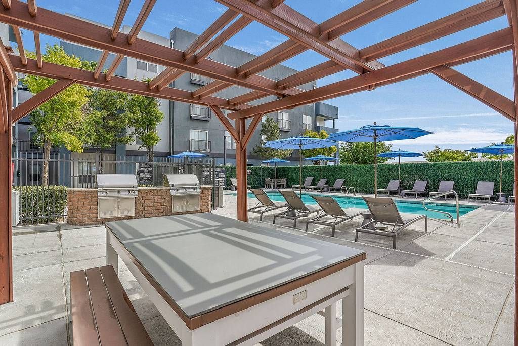 Outdoor pool area with lounge chairs, blue umbrellas, and a wooden pergola at Solaire Luxury Apartments, offering apartments for rent in Albuquerque, NM.