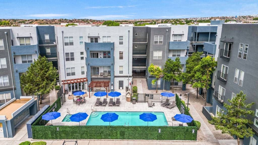 Communal pool area with blue umbrellas, lounge chairs, and modern apartment buildings around at Solaire Luxury Apartments, offering apartments for rent in Albuquerque, NM.