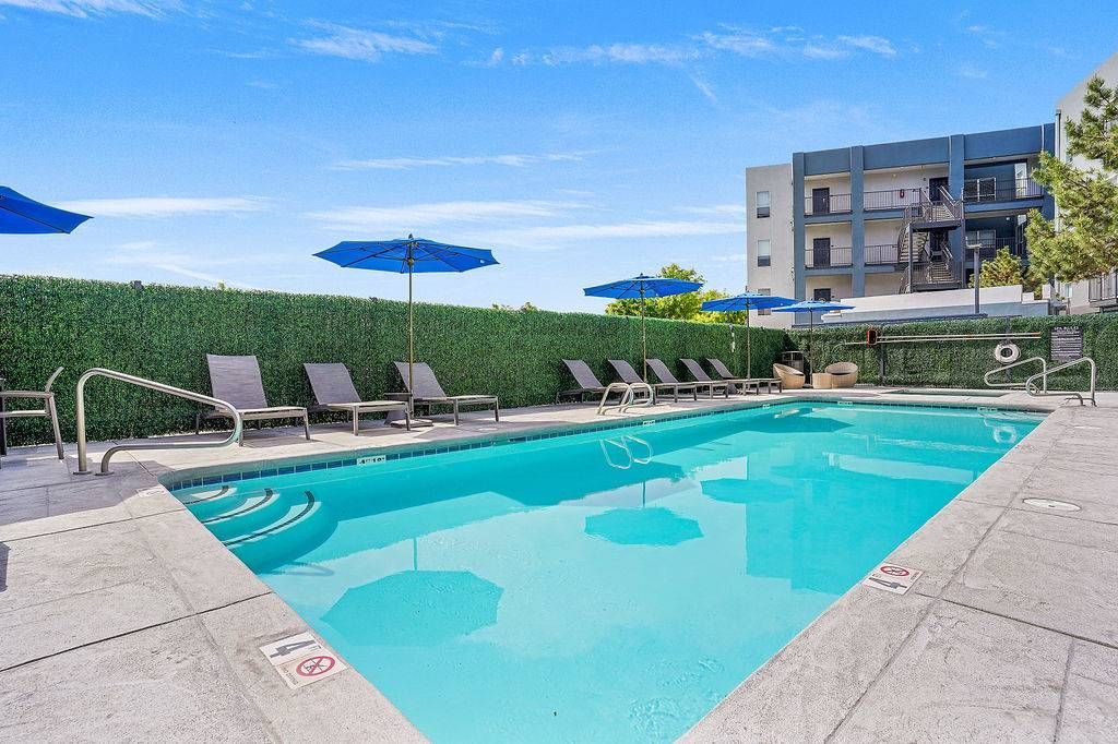 Outdoor pool area with lounge chairs and blue umbrellas at an apartment community at Solaire Luxury Apartments, offering apartments for rent in Albuquerque, NM.
