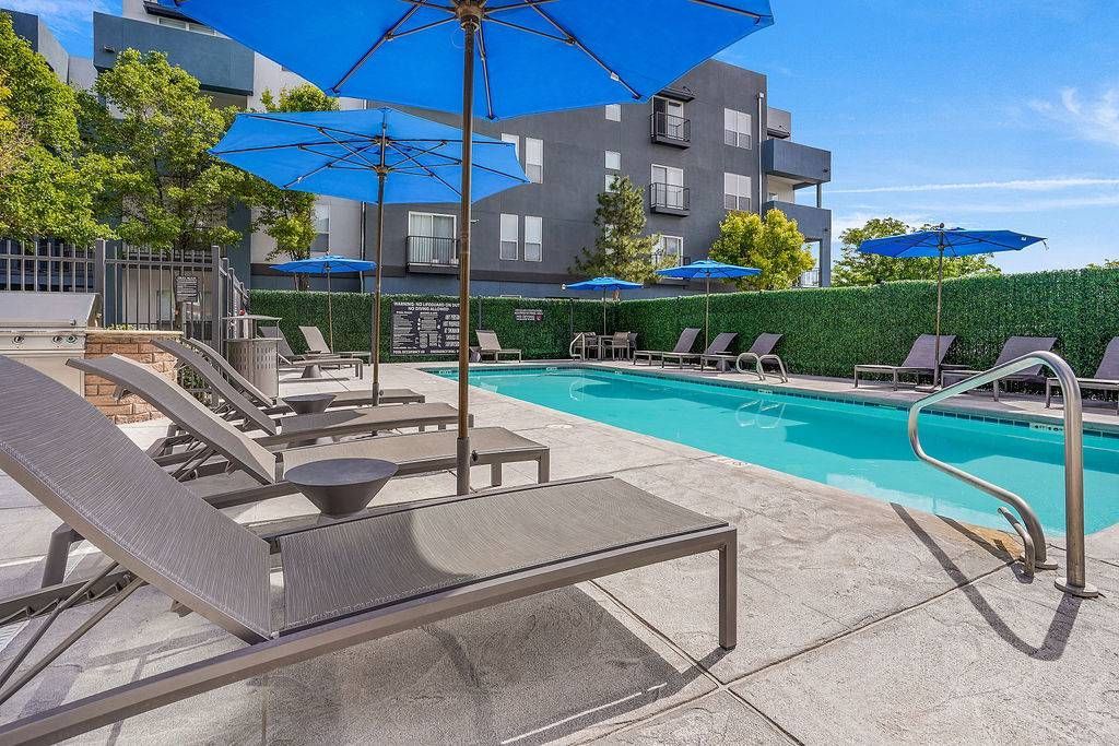 Outdoor pool area with lounge chairs, blue umbrellas, and a surrounding hedge at Solaire Luxury Apartments, offering apartments for rent in Albuquerque, NM.