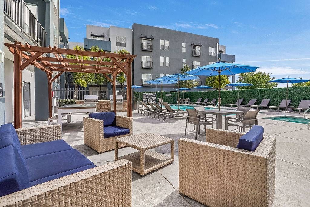 Outdoor apartment community pool deck with wicker seating, lounge chairs, umbrellas, and a pergola at Solaire Luxury Apartments, offering Albuquerque apartments for rent.