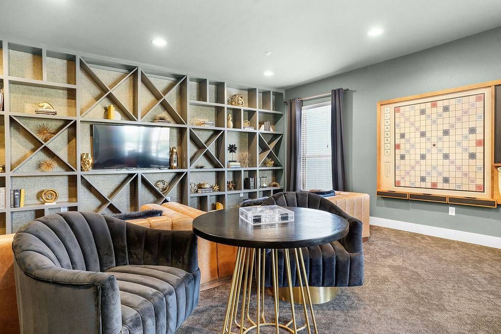 Indoor community lounge with a round table, plush curved chairs, TV, and wall shelving at Solaire Luxury Apartments, offering apartments in Albuquerque, NM.