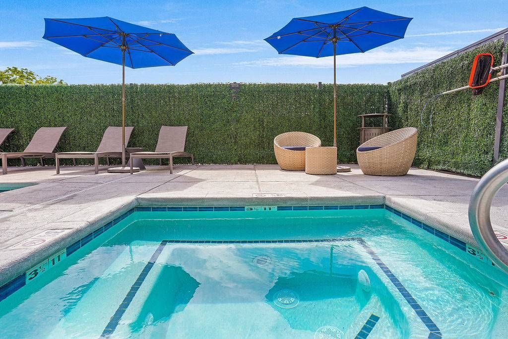 Outdoor pool area with blue umbrellas, lounge chairs, and wicker seating on a sunlit patio at Solaire Luxury Apartments, offering apartments for rent in Albuquerque, NM.