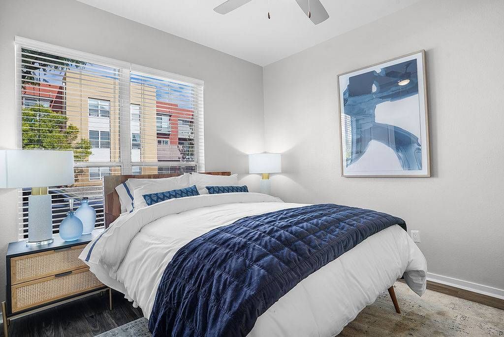 Bedroom at Solaire Luxury Apartments, offering Albuquerque apartments for rent with a queen bed, navy quilt, two nightstands, lamps, and a large window with blinds.