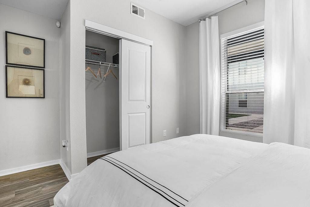 Bedroom with a white bed, open closet, and window with blinds at Solaire Luxury Apartments, offering Albuquerque apartments for rent.