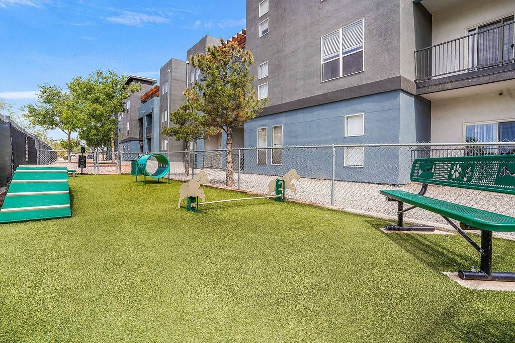 Community outdoor amenity with turf, fencing, benches, and play equipment beside an apartment building at Solaire Luxury Apartments, offering Albuquerque apartments for rent.
