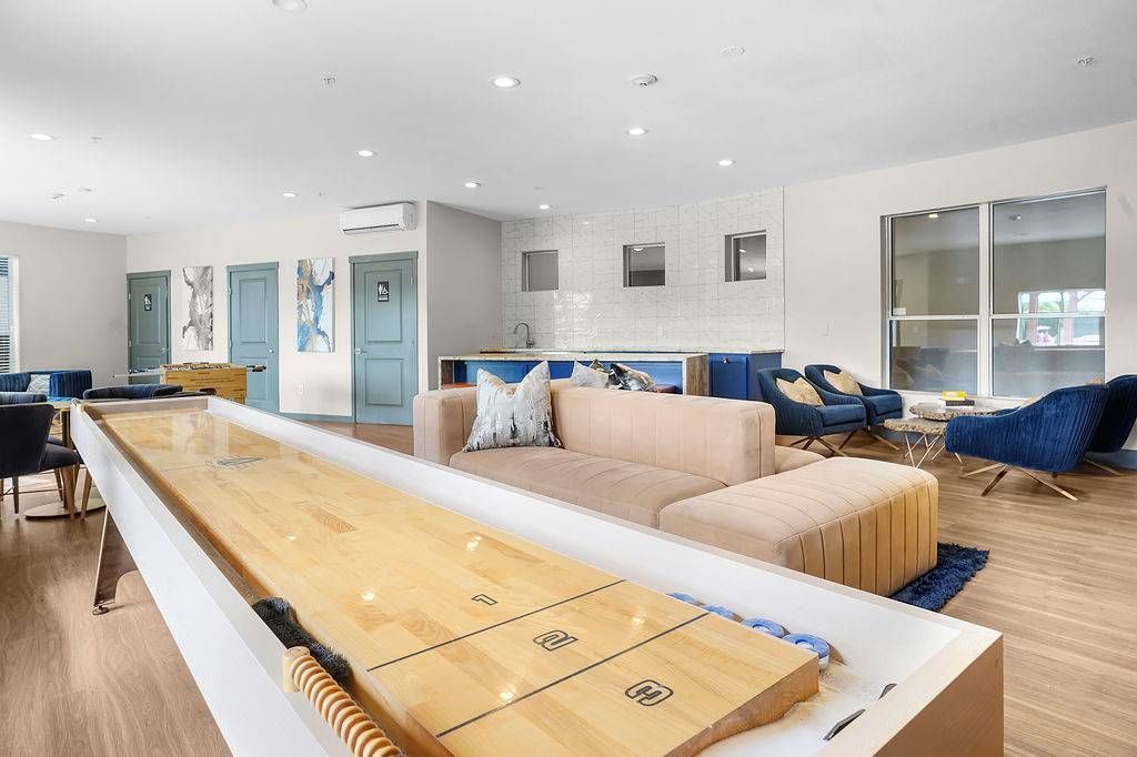 Indoor community lounge with beige sectional, blue chairs, and a long shuffleboard table at Solaire Luxury Apartments, offering apartments for rent in Albuquerque, NM.