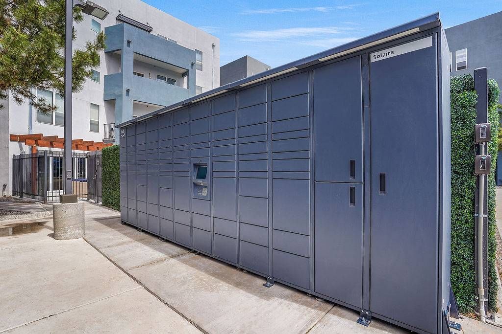 Exterior view of a long row of gray, external package lockers beside an apartment building at Solaire Luxury Apartments, offering Albuquerque apartments for rent.