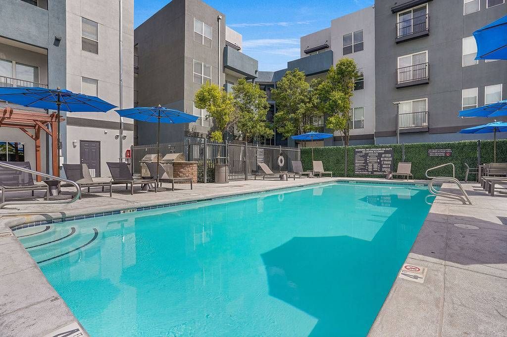 Outdoor apartment pool with lounge chairs and blue umbrellas at Solaire Luxury Apartments, offering apartments for rent in Albuquerque, NM.