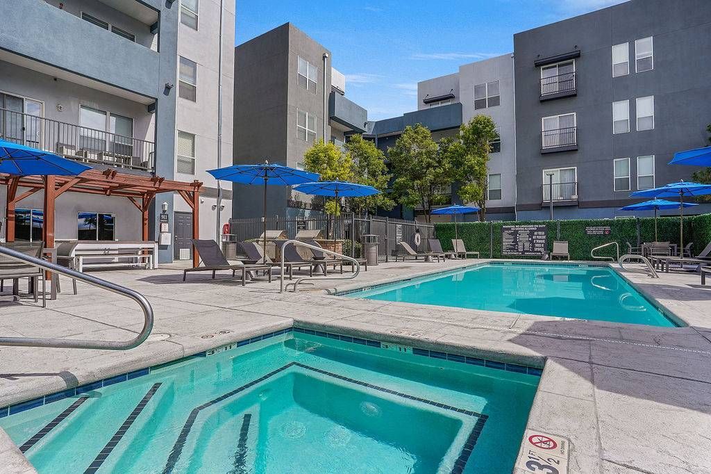 Outdoor community pool and hot tub area with blue umbrellas and lounge chairs at Solaire Luxury Apartments, offering apartments for rent in Albuquerque, NM.